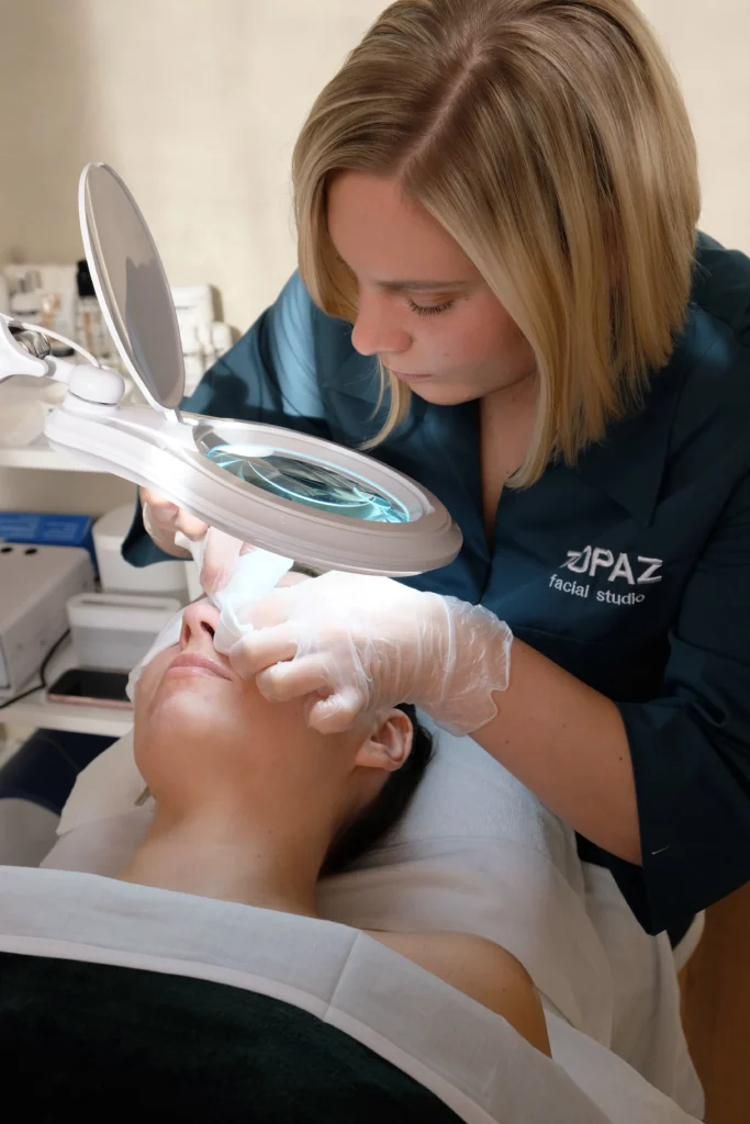 Esthetician examining a client's skin under a magnifying lamp.