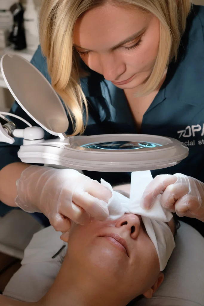 Topaz practitioner examining a client’s skin under a magnifying lamp.